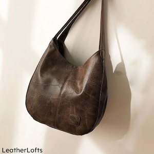 May include: A brown leather shoulder bag with a patchwork design. The bag has a curved shape and long straps. The text "LeatherLofts" is visible at the bottom left of the image.