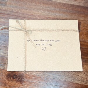 May include: A brown paper envelope tied with twine and a handwritten message that reads "open when the day was just way too long" with a small heart drawn below the text.