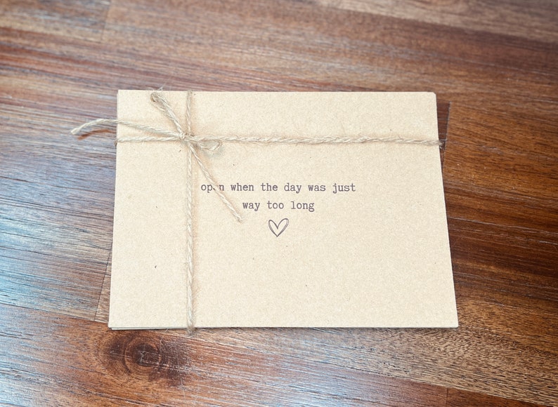 May include: A brown paper envelope tied with twine and a handwritten message that reads "open when the day was just way too long" with a small heart drawn below the text.