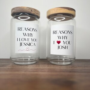 May include: Two clear glass jars with wooden lids. Each jar has a white label with the text "Reasons Why I Love You" and a name, "Jessica" and "Josh".