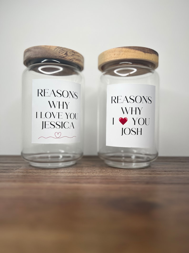 May include: Two clear glass jars with wooden lids. Each jar has a white label with the text "Reasons Why I Love You" and a name, "Jessica" and "Josh".