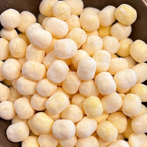 Puede incluir: Primer plano de un montón de pequeños caramelos redondos de color amarillo pálido. Los caramelos tienen una forma ligeramente irregular y un acabado mate. La impresión general es de un dulce.
