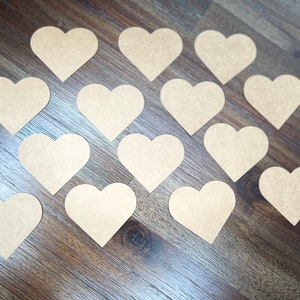 May include: A collection of 15 brown paper heart shapes arranged in a circular pattern on a wood surface.