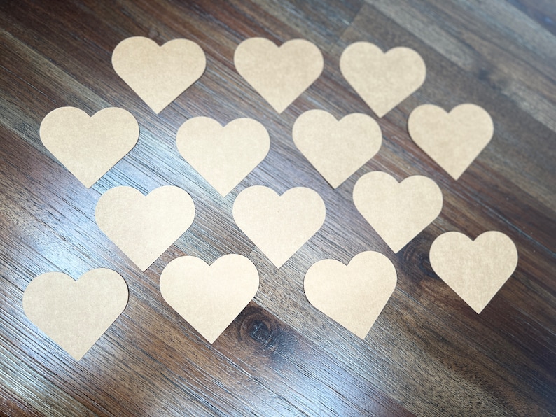 May include: A collection of 15 brown paper heart shapes arranged in a circular pattern on a wood surface.