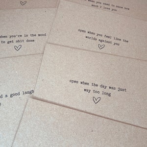 May include: A set of brown paper envelopes with handwritten messages on them. The messages include "open when you're in the mood to get shit done", "open when you need to know how much I love you", "open when you feel like the worlds against you", "open when the day was just way too long", and "open when you need a good laugh".