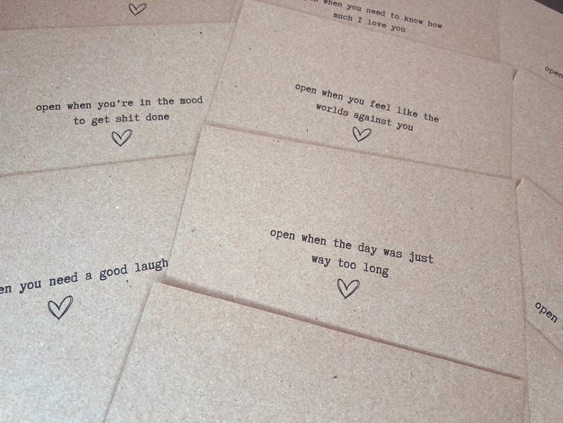 May include: A set of brown paper envelopes with handwritten messages on them. The messages include "open when you're in the mood to get shit done", "open when you need to know how much I love you", "open when you feel like the worlds against you", "open when the day was just way too long", and "open when you need a good laugh".