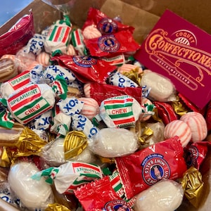 May include: A box overflowing with assorted candies, including spearmint chews, wrapped candies, and red packages of Uncle Joe's Mint Balls. A maroon box with gold lettering that reads "Coquet Confectioners" is also visible.