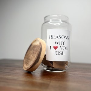 May include: A glass jar with a wooden lid filled with small pieces of paper. The jar has a label that says "Reasons Why I &hearts; You Josh".