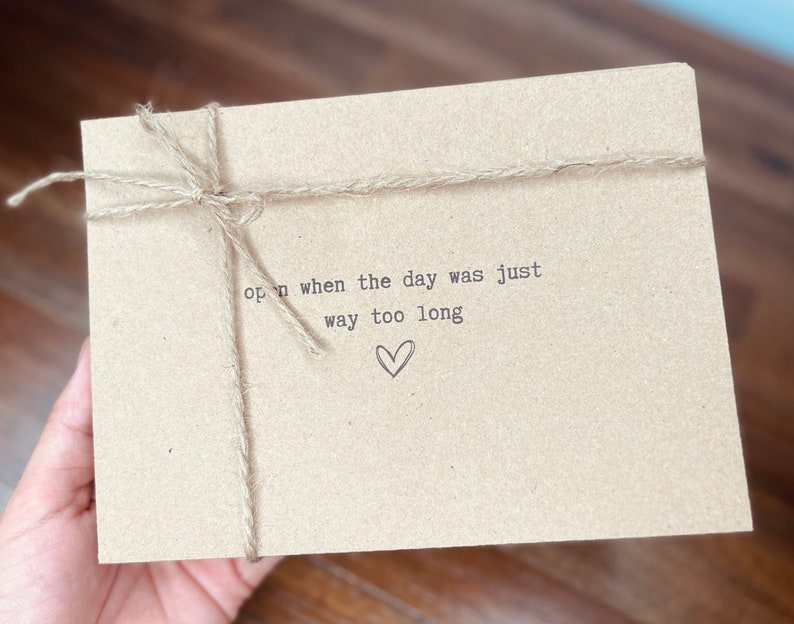 May include: A brown paper envelope with twine tied around it. The envelope has the text "open when the day was just way too long" written on it with a small heart drawn below the text.