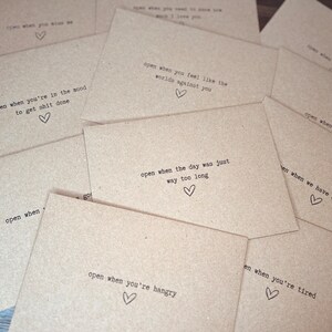 May include: A set of brown paper envelopes with handwritten messages on them. Each envelope has a different message, such as "open when you're in the mood to get stuff done" or "open when you feel like the world's against you".