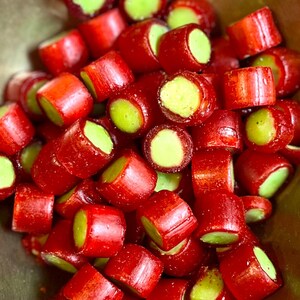 Könnte beinhalten: Nahaufnahme eines Haufens roter und grüner Süßigkeiten. Die Süßigkeiten sind zylindrisch mit einem leuchtend roten Äußeren und einem hellgrünen Kern. Die Süßigkeiten sind in einem Haufen angeordnet, wobei einige Stücke geschnitten sind, um den grünen Kern freizulegen.