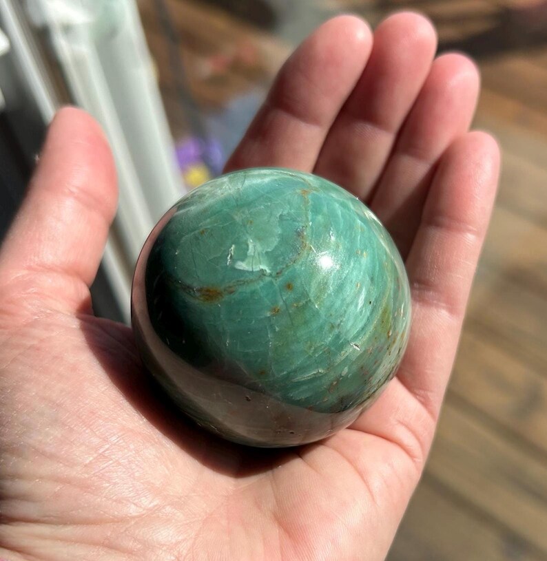 Puede incluir: Una esfera verde y marr&oacute;n de piedra serpentina pulida. La esfera tiene un acabado liso y brillante con intrincados patrones de verde y marr&oacute;n que se arremolinan.