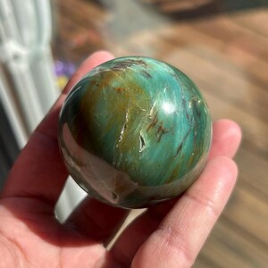 Puede incluir: Una esfera de jaspe pulido, una variedad de piedra preciosa, de color verde y marr&oacute;n con patrones de remolino y un acabado brillante.