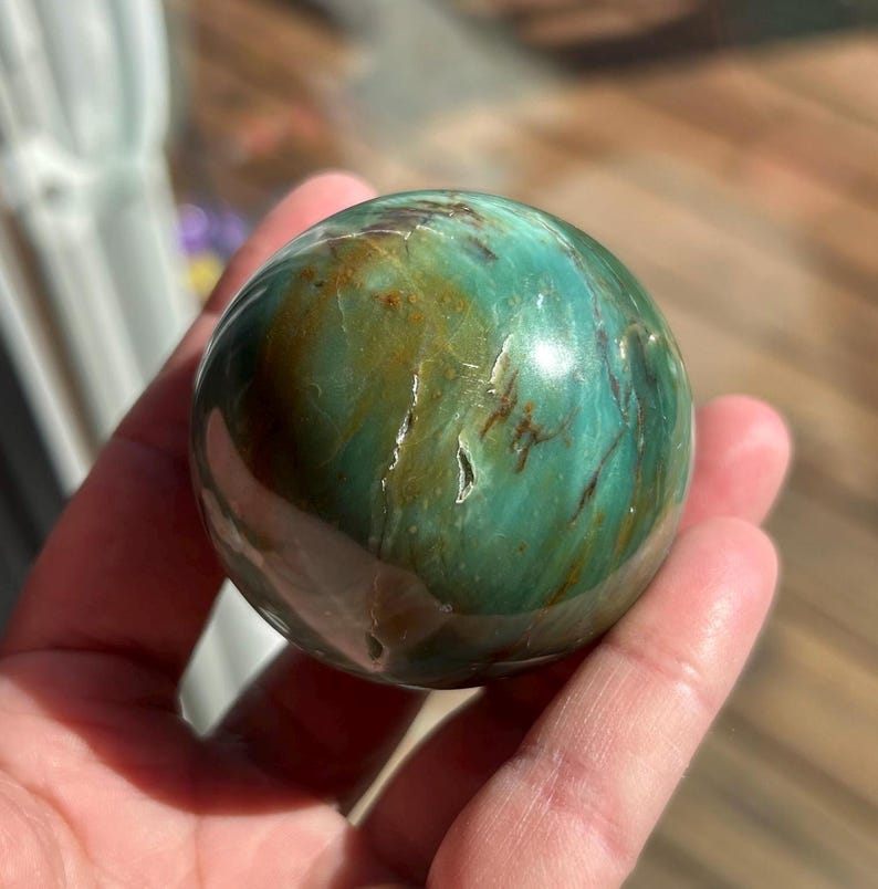 Puede incluir: Una esfera de jaspe pulido, una variedad de piedra preciosa, de color verde y marr&oacute;n con patrones de remolino y un acabado brillante.