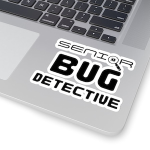 May include: A white sticker with black text that reads "Senior Bug Detective" with a magnifying glass icon and a bug icon. The sticker is on a silver laptop.