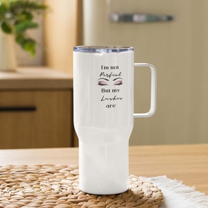 May include: White insulated tumbler with a handle and a clear lid. The tumbler has the text "I'm not perfect but my lashes are" with an illustration of eyelashes. The tumbler is on a woven placemat.