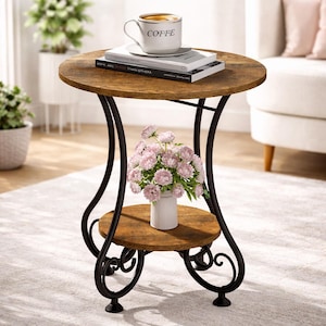 May include: A round, two-tiered side table with a distressed wood finish. The table has black metal legs with decorative scrollwork. A white coffee cup with "COFFEE" printed on it sits on top, along with books and a vase of pink flowers.
