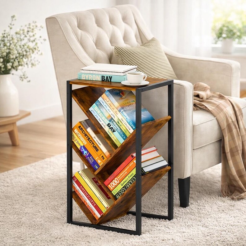 Puede incluir: Una mesa auxiliar marr&oacute;n y negra con una estanter&iacute;a incorporada. La mesa tiene una estructura met&aacute;lica y estantes de madera en &aacute;ngulo llenos de libros. Una taza de caf&eacute; y libros est&aacute;n encima de la mesa. La mesa est&aacute; al lado de un sill&oacute;n beige.