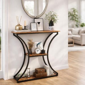 May include: A rustic console table with a dark metal frame and two wooden shelves. The top shelf holds decorative items like a vase, candle, and framed art. The table is against a white wall with a mirror above it.