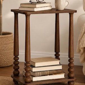 May include: A rectangular dark brown wooden side table featuring four turned legs with a stacked ball design. The table has a flat top surface and a lower shelf. Two books and a pair of glasses sit on the top, while four books are stacked on the lower shelf.
