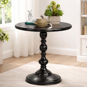 May include: A black, round side table with a decorative pedestal base. The table is topped with a small white deer figurine, a cup and saucer, and a small potted plant. The table is approximately 24 inches in diameter.