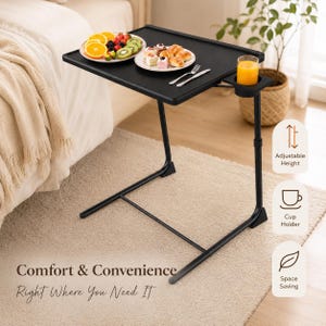 May include: A black rectangular C-shaped side table with a matte finish, featuring a built-in circular cup holder on the side. The table surface holds two white plates with fruit and pastries, a glass of orange juice, and two silver forks.