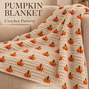 Puede incluir: Una manta de ganchillo de color crema con un patrón repetitivo de pequeñas calabazas naranjas con tallos verdes. El texto PUMPKIN BLANKET Crochet Pattern y KAEMORE es visible. La manta tiene un diseño texturizado de punto acanalado.