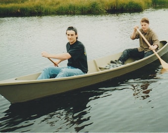 May include: Two people in a green canoe on a lake. The person in the front is paddling with a wooden paddle. The person in the back is holding a wooden paddle.