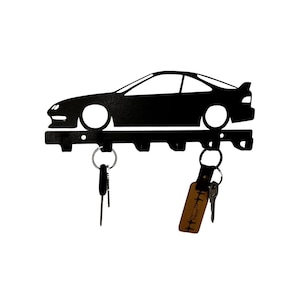Könnte beinhalten: Schwarzer Schlüsselhalter aus Metall in Form eines Autos. Der Schlüsselhalter hat fünf Haken zum Aufhängen von Schlüsseln. An den Haken hängen zwei Schlüsselsätze.