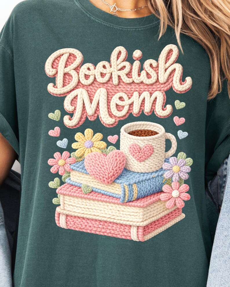 May include: Dark teal t-shirt with the words "Bookish Mom" in a 3D knit design. The graphic includes a stack of books, a coffee mug, hearts, and flowers, all in a soft, pastel color palette.