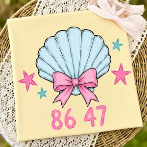 Könnte beinhalten: Eine quadratische, hellgelbe Leinwand mit einem handgemalten Muscheldesign. Die Muschel ist hellblau mit einer rosa Schleife. Rosa und blaue Sterne umgeben die Muschel, und die Zahlen "86 47" stehen darunter in Rosa.