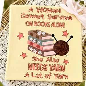 Può includere: Stampa su tela con la scritta "A Woman Cannot Survive On Books Alone She Also Needs Yarn A Lot of Yarn." L'immagine presenta una pila di libri, filato e stelle in un design stravagante. Lo sfondo è di colore giallo chiaro.