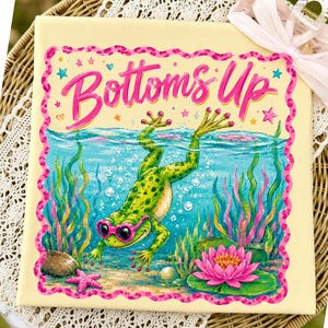 Könnte beinhalten: Quadratischer Leinwanddruck mit einer Illustration eines grünen Frosches mit rosa Sonnenbrille unter Wasser. Die Worte "Bottoms Up" sind in rosa Schrift geschrieben. Das Kunstwerk zeigt einen rosa und gelben Rahmen, Blasen und eine rosa Seerose.