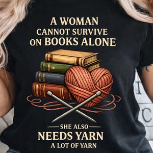 Könnte beinhalten: Schwarzes T-Shirt mit dem Text "A Woman Cannot Survive on Books Alone, She Also Needs Yarn A Lot of Yarn." Die Grafik zeigt einen Stapel Bücher und einen herzförmigen Wollknäuel mit Stricknadeln.