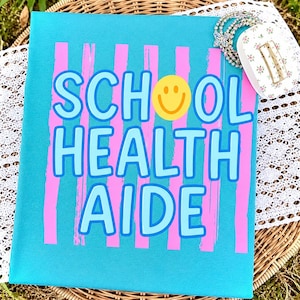 Könnte beinhalten: Ein türkisfarbenes T-Shirt mit den Worten "SCHOOL HEALTH AIDE" in Hellblau, umrandet von dunklerem Blau. Rosa vertikale Streifen und ein gelbes Smiley-Gesicht sind ebenfalls abgebildet. Ein Armband und eine Haarspange mit Blumen befinden sich rechts.