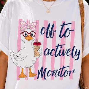 Könnte beinhalten: Weißes T-Shirt mit einer Cartoon-Ente, die eine Brille und eine Schleife trägt und ein Getränk hält. Das Design umfasst rosa Streifen und den Text "off to actively monitor" in marineblauer Schrift.