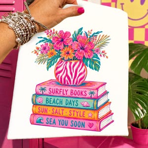 Könnte beinhalten: Weißer Leinwanddruck mit einem farbenfrohen Blumenarrangement in einer zebra gemusterten Vase, auf einem Stapel von Büchern. Die Bücher tragen die Titel "Surfly Books", "Beach Days", "Sun Salt Style" und "Sea You Soon", mit Strand-Illustrationen.