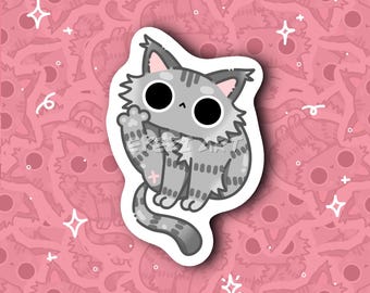 Puede incluir: Una pegatina de gato gris con grandes ojos negros y una pata levantada. El gato tiene un patrón de rayas y una cruz rosa en la pata. La pegatina está delineada en blanco y colocada sobre un fondo rosa con caras de gato y estrellas repetidas.