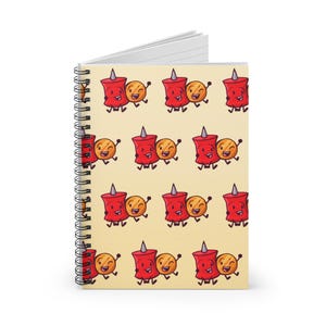 Op de afbeelding: Een spiraalgebonden notitieboek met een herhalend patroon van cartoon-punaise en lachende cirkels op een crèmekleurige achtergrond. De punaises zijn rood met een grijze punt en de cirkels zijn geeloranje. Het notitieboek heeft een witte binnenkant.