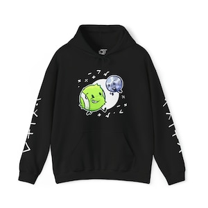 Pode incluir: Camisola de capuz preta com um desenho de personagem de banda desenhada verde e azul. As personagens são uma bola de ténis e um planeta. A camisola tem texto branco nas mangas.