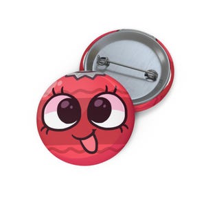 Pode incluir: Um botão vermelho com um rosto de desenho animado. Apresenta olhos grandes, uma boca sorridente e uma língua de fora. O botão tem uma parte traseira de metal e um alfinete. O design é divertido e caprichoso.