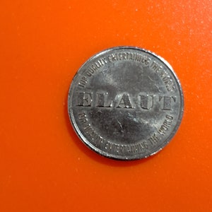 May include: A silver token with the words "Top Quality Entertain the World" and "Elaut" printed on it.