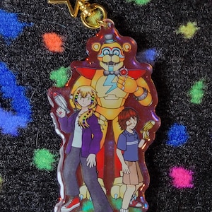 May include: A colorful acrylic keychain featuring characters from a video game. The design includes a large, golden bear-like figure with a lightning bolt, and two smaller figures holding ray guns. The keychain has a gold star-shaped clasp.