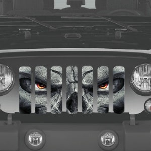 Puede incluir: Un Jeep Wrangler negro con una rejilla de superposición de calavera y huesos cruzados. La calavera tiene ojos rojos y una expresión amenazante.