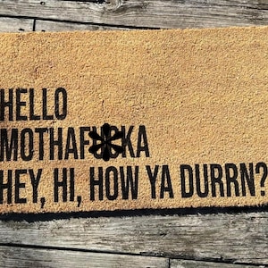 May include: A brown doormat with the text "HELLO MOTHAF*KA HEY, HI, HOW YA DURRN?" in black lettering.