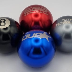 May include: Four metallic spheres in black, red, blue, and grey. The black sphere has an 8 ball design. The red sphere has the text "E86 SCHNELLMASCHINE". The blue sphere has "DUB" and a star. The grey sphere has "TOTAL PETROLHEAD".