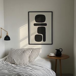 Könnte beinhalten: Ein minimalistisches Schlafzimmer mit einem Bett mit schwarz-weiß gestreifter Bettwäsche. Ein gerahmtes abstraktes Kunstwerk hängt an der Wand. Ein kleiner Holztisch trägt eine schwarze Kanne und eine weiße Tasse.