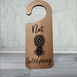 May include: A wooden door hanger with a pineapple design and the text "Not Sleeping".