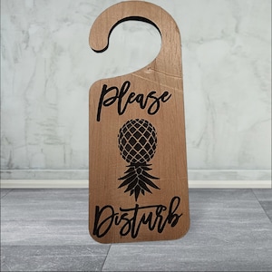 May include: A wooden door hanger with a pineapple design and the text "Please Disturb".