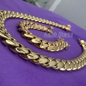 May include: A gold chain necklace and bracelet set with a thick, chunky curb link design. The set is made of gold-plated metal and features a shiny, polished finish.